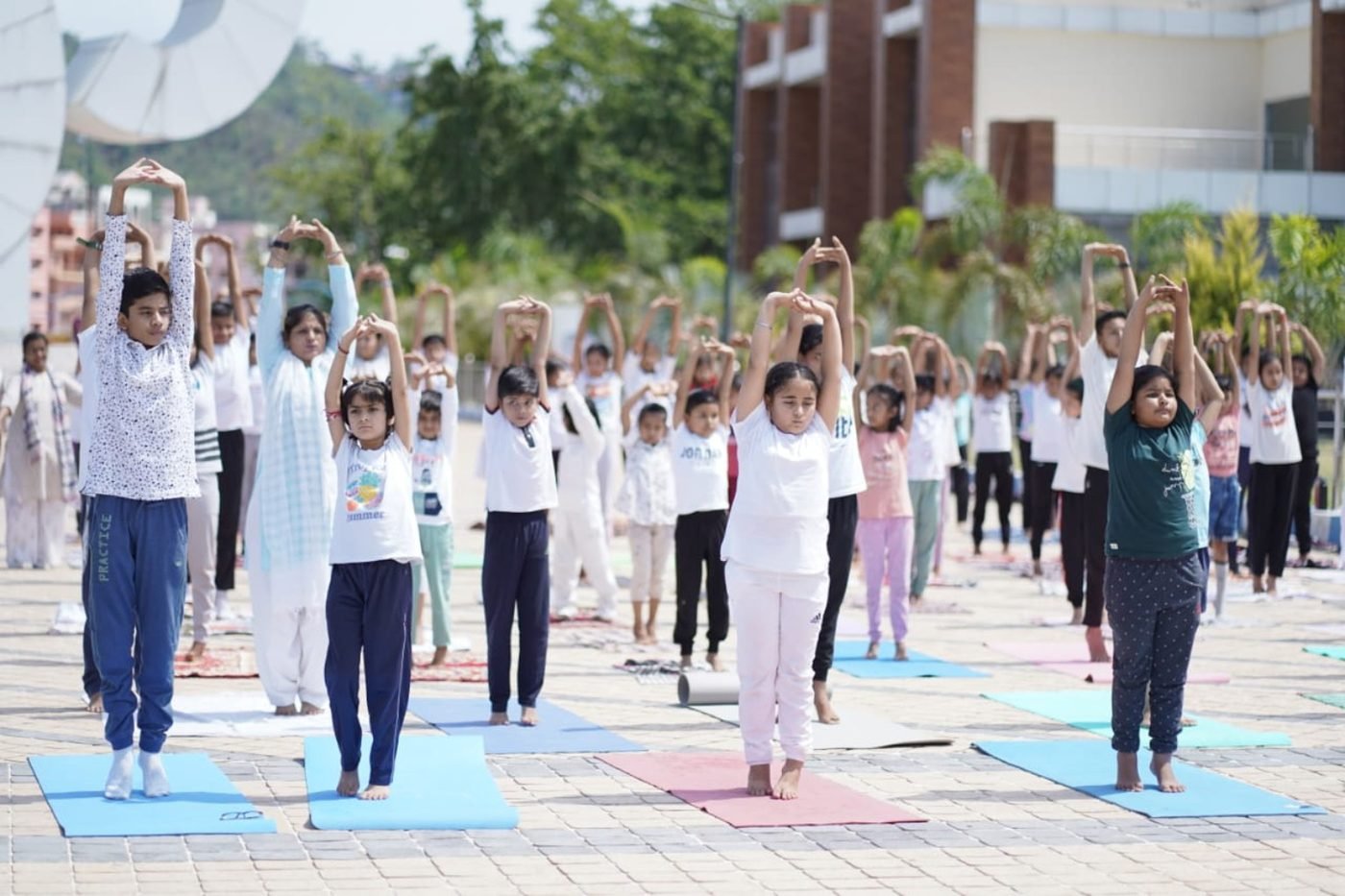 A large outdoor community yoga session with children practising together, marking International Yoga Day
